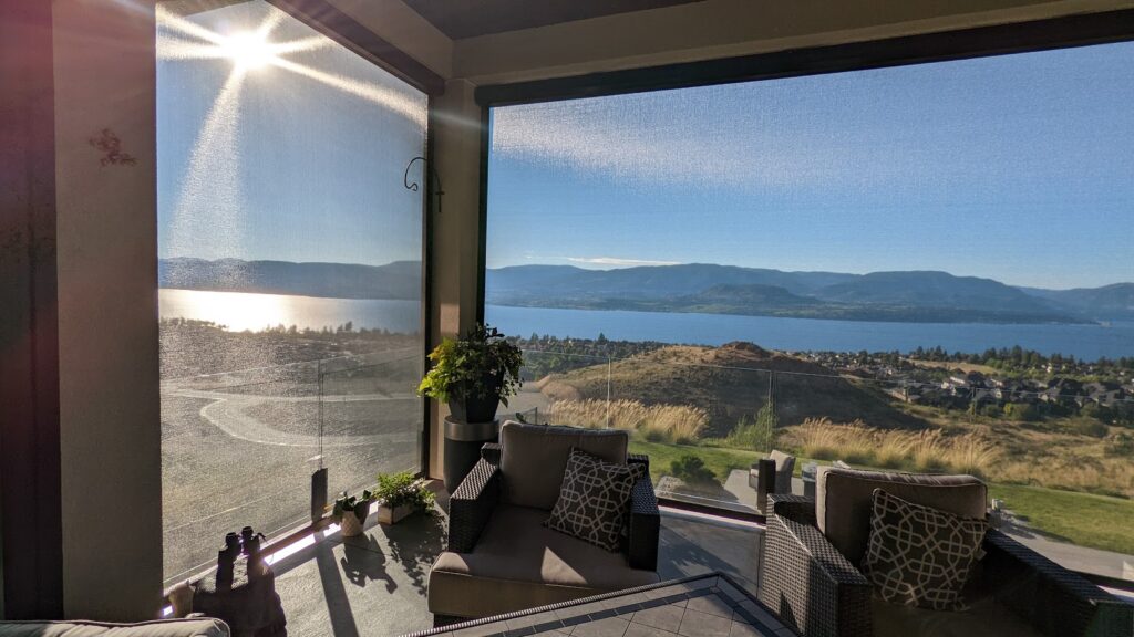 Retractable screen on a patio with a stunning view of a lake, mountains, and sunset, providing shade while maintaining a clear scenic view